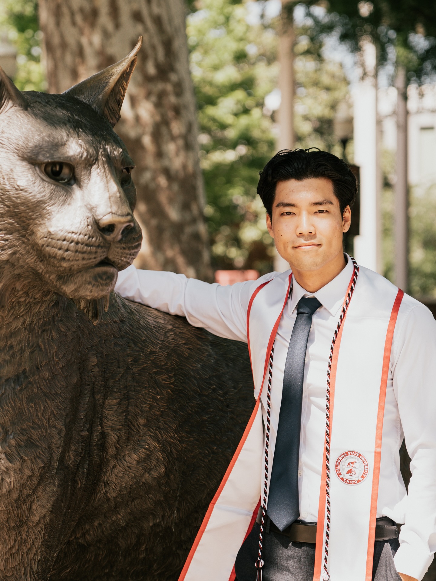 Graduate in a Chico State stole resting a hand on the bronze Wildcat statue
