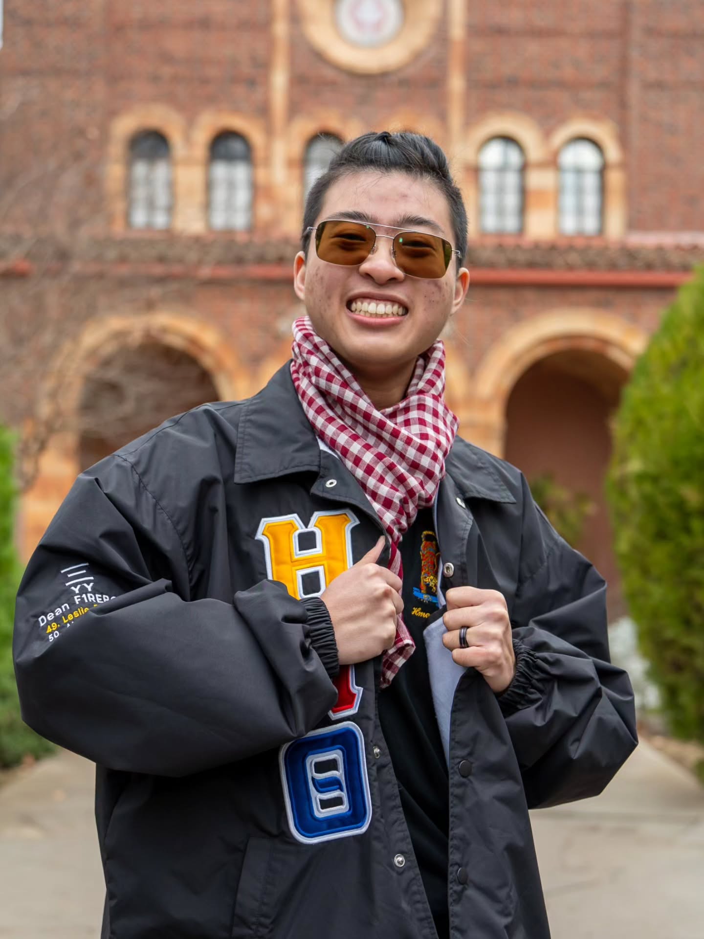 Chapter member in sunglasses and a gingham scarf grinning in front of a brick arcade