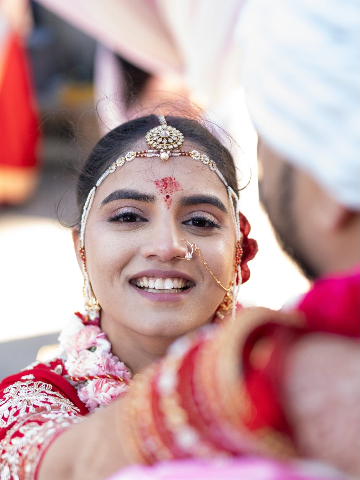 Bride in gold jewelry and a nose ring smiling at the camera, red bangles in the foreground